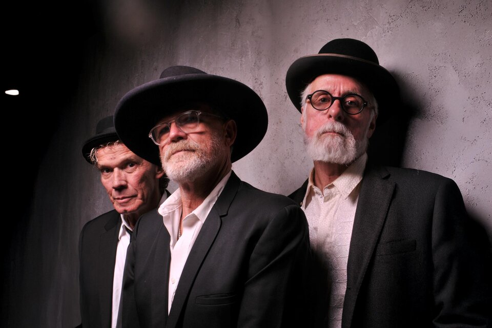 Drei Männer in dunklen Anzügen und schwarzen Hüten posieren vor einer grauen Wand; zwei tragen Brille und haben grauen Bart, alle blicken ernst in die Kamera. | © Burtscher