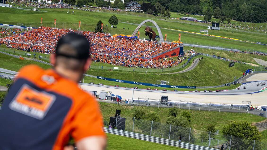 Ein großer Motorsport-Event mit vielen Zuschauern in orangefarbener Kleidung. Im Hintergrund ist die Rennstrecke und die malerische Landschaft zu sehen. | © Lucas Pripfl - Red Bull Ring