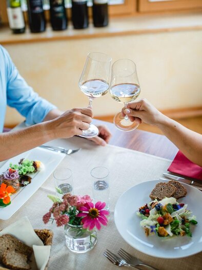A romantic dinner with two people toasting their glasses. On the table are freshly prepared dishes and a flower decoration. | © Karin Bergmann