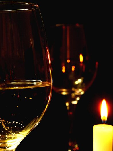 An elegant glass with a drink is in the foreground. In the background, candles glow in the darkness. | © pixabay