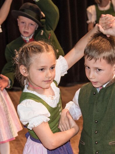 Two children are dancing in traditional costumes. In the background, there are other children watching the dance. | © Narzissenfest/Herbert Sambs