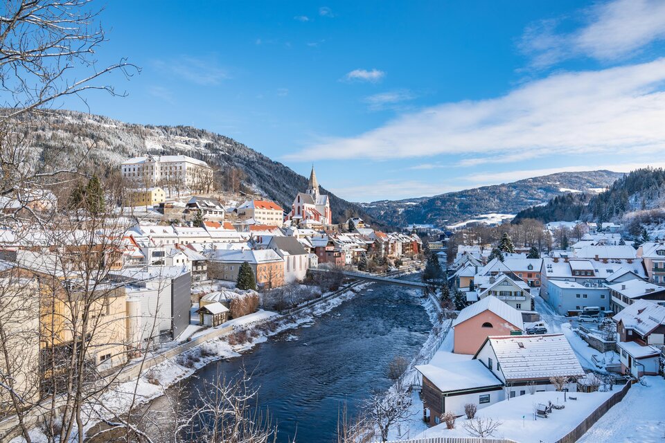 Eine verschneite Stadt am Fluss mit bunten Häusern und Bergen im Hintergrund. Der Himmel ist klar und blau. | © Tv Murau