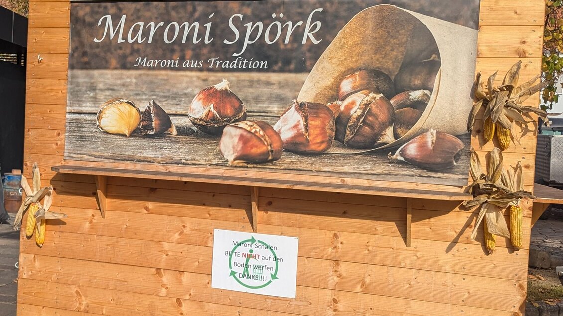 Ein Holzstand mit einem Banner, das geröstete Maronen zeigt. Darunter steht "Maroni Spörk – Maroni aus Tradition". | © PStossier
