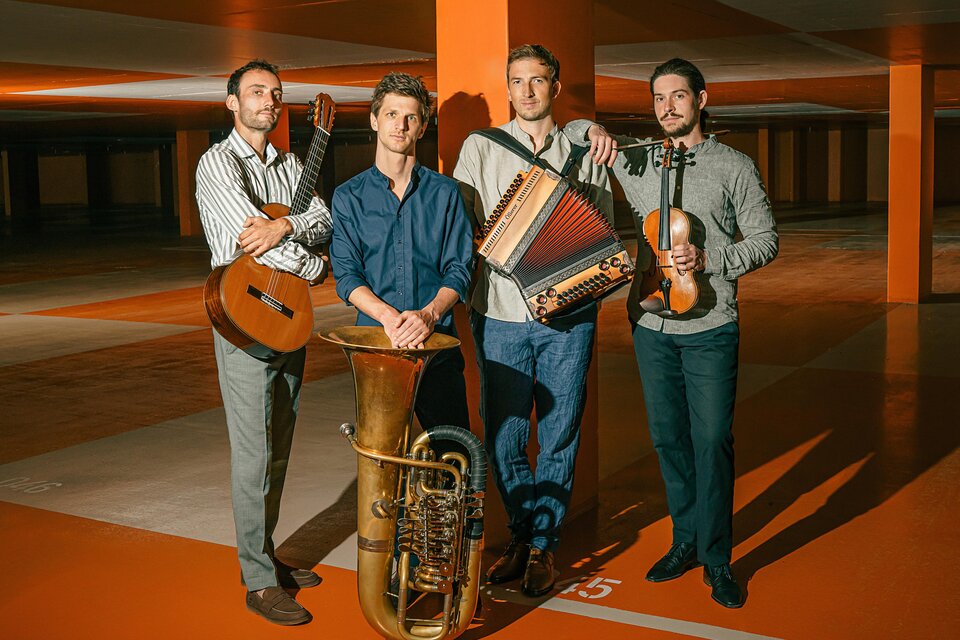 Vier Musiker posieren in einer orange beleuchteten Tiefgarage: links mit Gitarre, in der Mitte ein großes Blechblasinstrument (Tuba) am Boden, daneben ein Musiker mit Steirischer Harmonika, rechts ein Musiker mit Geige in der Hand. | © Maxjoseph