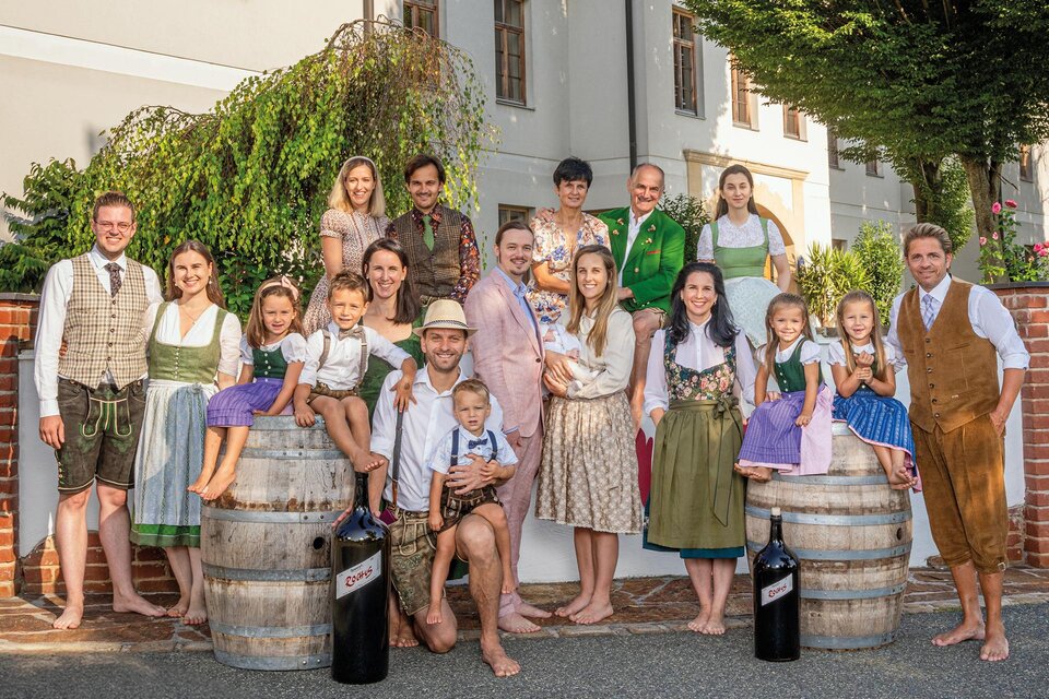 Eine Gruppe von Menschen in traditioneller Tracht steht vor einem Gebäude. Sie lächeln und posieren um Holzfässer.