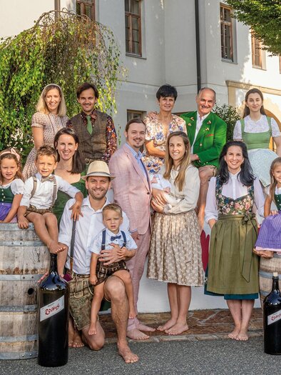 A group of people in traditional costumes stands in front of a building. They smile and pose around wooden barrels.
