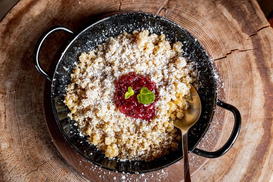 Ein gefüllter Teller mit süßem Grießbrei, bestreut mit Puderzucker und einer Portion Marmelade. Eine frische Minzeblattgarniert das Gericht. | © Martin Huber