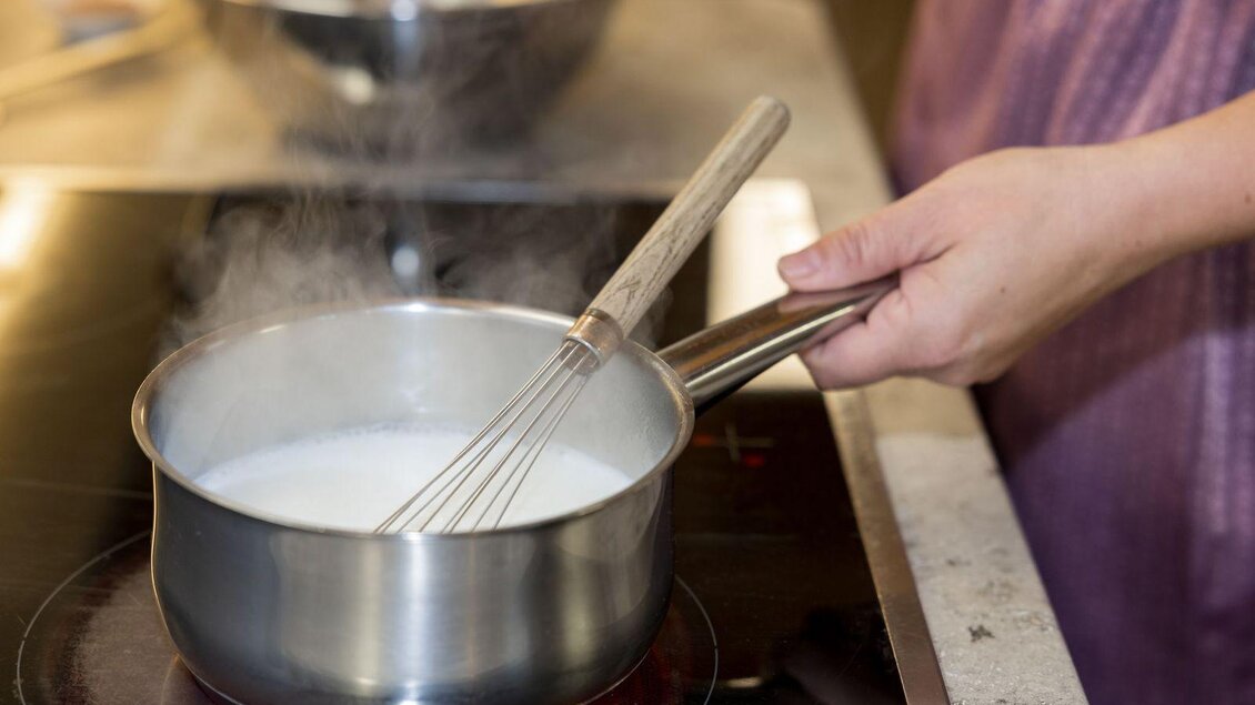 Ein Topf mit kochender Milch auf dem Herd. Eine Person rührt mit einem Schneebesen in dem Topf. | © Martin Huber