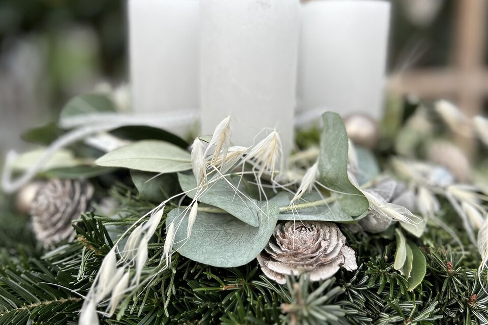 Ein festlicher Tischkranz mit drei weißen Kerzen, umgeben von grünen Blättern und dekorativen Elementen. Der Kranz vermittelt eine gemütliche, einladende Atmosphäre. | © Elisabeth Micko