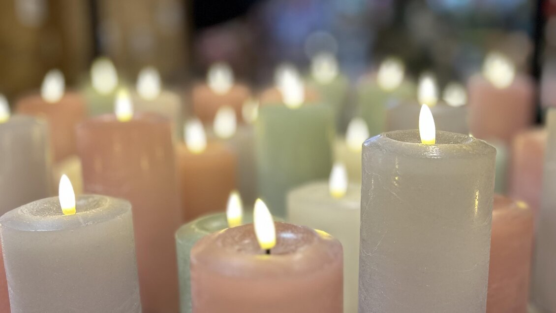 Bunte Kerzen in verschiedenen Farben leuchten sanft. Sie stehen auf einem Holzregal und schaffen eine gemütliche Atmosphäre. | © Elisabeth Micko