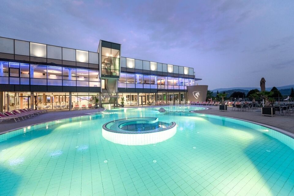 Ein modernes Hotel mit einem großen Pool. Der Pool hat eine runde Whirlpool-Ecke und ist bei Dämmerung beleuchtet. | © Region Graz-Die Abbilderei