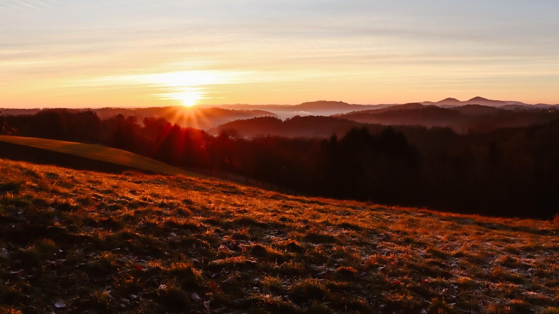 Ein schöner Sonnenaufgang über sanften Hügeln. Der Himmel ist in warmen Farben erleuchtet.