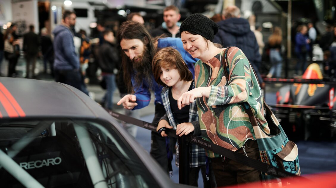 Eine Familie schaut sich interessiert ein Auto auf einer Messe an. Sie zeigen mit dem Finger auf das Fahrzeug und scheinen begeistert. | © Valerie_Maltseva