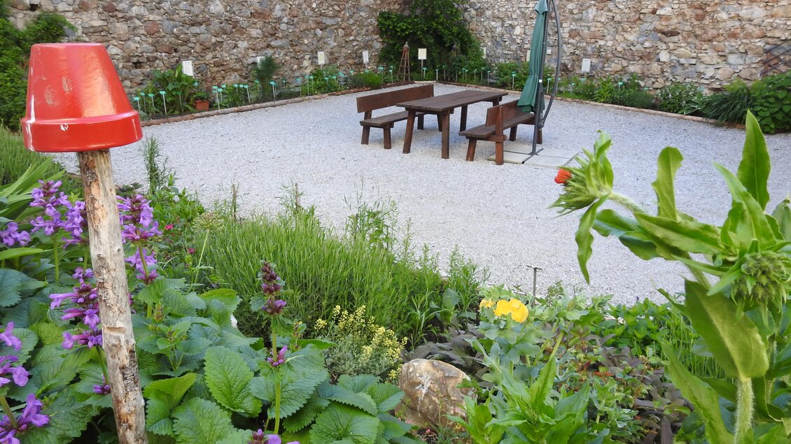 Ein schöner Garten mit bunten Blumen und einem Kiesbereich. In der Mitte steht ein Tisch mit Stühlen und einem Sonnenschirm. | © Naturpark Sölktäler