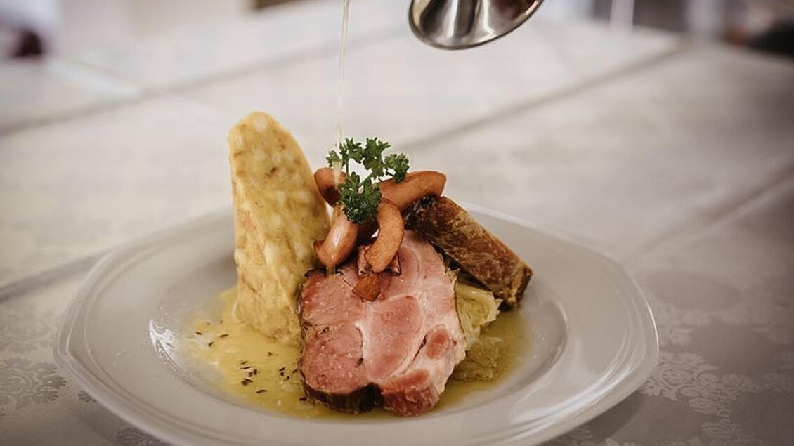 Ein appetitlicher Teller mit zartem Fleisch, Beilagen und einer Sauce. Oben garnieren einige kleine Gemüse und ein Kräuterzweig. | © Martinhof