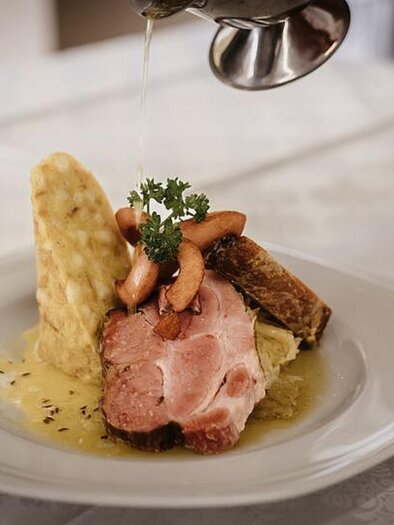 A delicious plate with tender meat, side dishes, and a sauce. On top, some small vegetables and an herb sprig are garnished. | © Martinhof