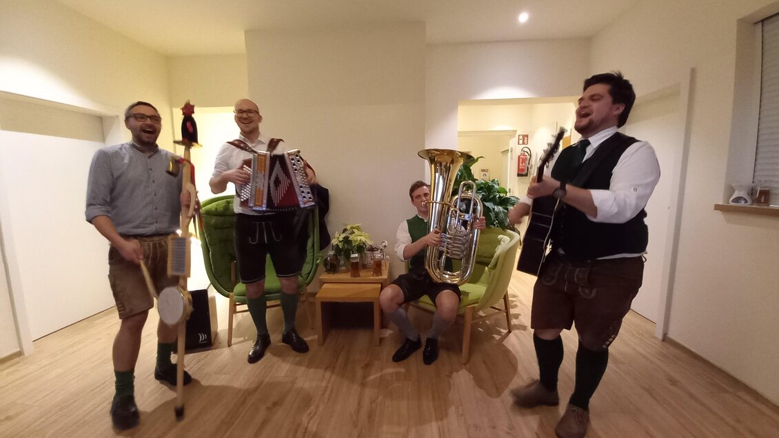 Eine Gruppe von vier Männern in traditioneller bayerischer Tracht spielt Musikinstrumente in einem hellen Raum. Sie haben Spaß und strahlen Begeisterung aus. | © Martinhof