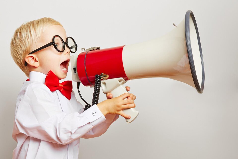 Ein kleiner Junge mit einer roten Fliege und einer weißen Bluse schreit in ein Megaphon. Er trägt große schwarze Brillen und zeigt viel Begeisterung. | © TV Südsteiermark - Robert  Kneschke