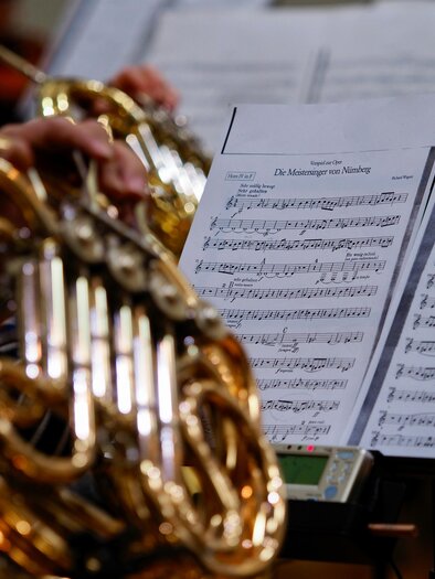 A musician is playing a French horn. In the background, sheet music with musical notation is visible. | © kazuo-ota-unsplash