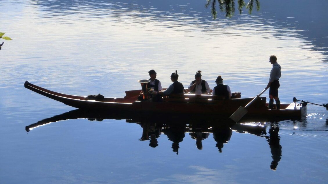 Eine Gruppe von Personen paddelt in einem traditionellem Boot auf einem ruhigen See. Die Weite des Wassers spiegelt die Umgebung wider. | © Fremdenverkehrsverein Altaussee