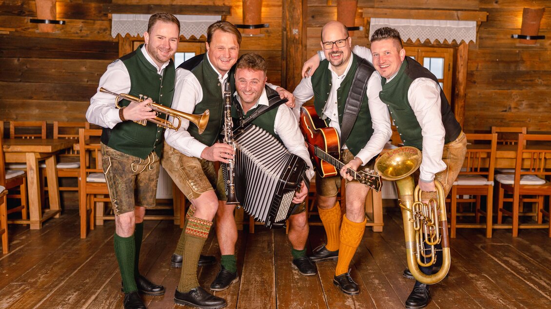 Eine Gruppe von fünf Musikern in traditionellen Trachten überträgt eine fröhliche Atmosphäre. Sie spielen verschiedene Instrumente in einem gemütlichen, rustikalen Raum. | © Markus Ponhold