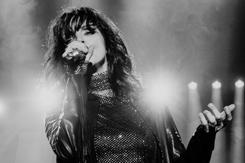 Eine Sängerin auf der Bühne mit einem Mikrofon in der Hand. Die Beleuchtung im Hintergrund schafft eine dramatische Atmosphäre. | © Sarah Rechbauer