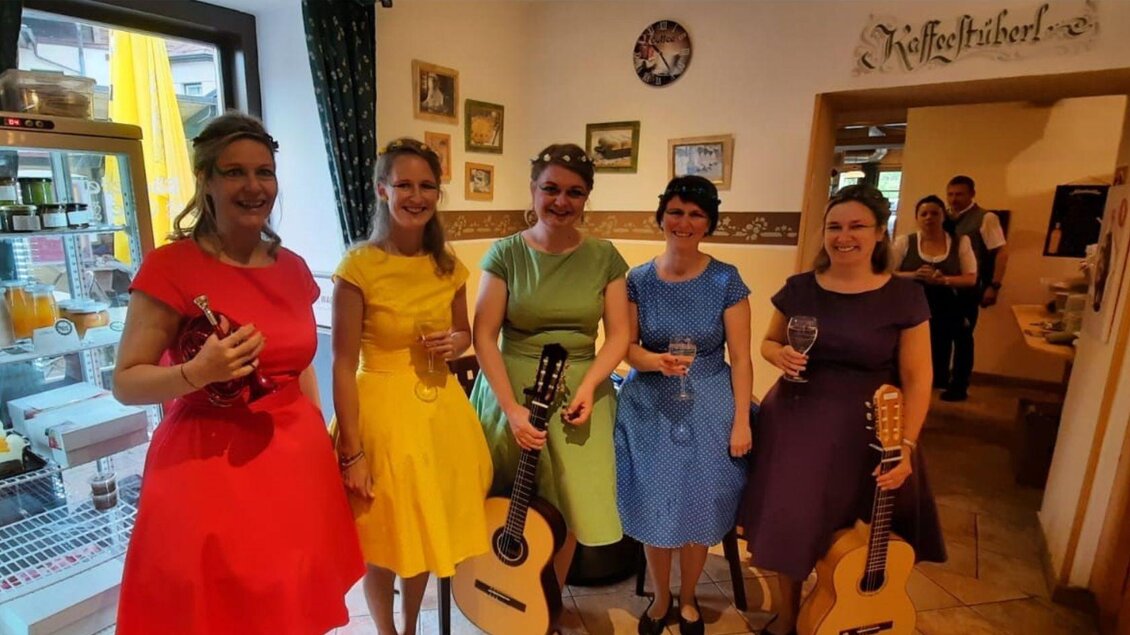 Eine Gruppe von fünf Frauen in bunten Kleidern hält Gitarren und Gläser. Sie stehen in einem gemütlichen Raum mit Bildern an den Wänden. | © Rainer Fischer