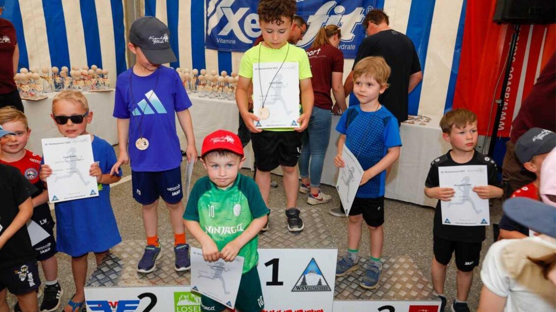 Eine Gruppe junger Kinder steht auf einem Siegertreppchen und hält Urkunden in der Hand. Sie tragen sportliche Kleidung und lächeln in die Kamera. | © Kainzinger Erich