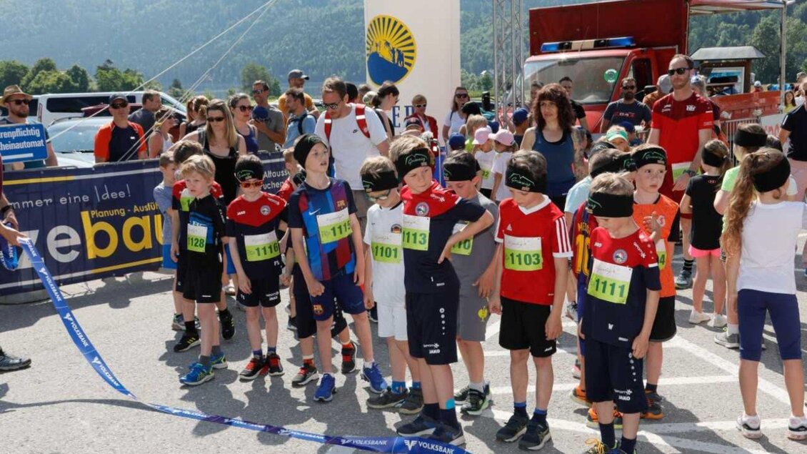 Eine Gruppe von Kindern steht am Start eines Wettlaufs. Im Hintergrund sind Zuschauer und eine festliche Atmosphäre zu sehen. | © Kainzinger Erich