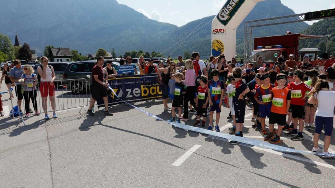 Eine Gruppe von Kindern steht bereit am Start eines Wettlaufs. Im Hintergrund sind Berge und Zuschauer zu sehen. | © Kainzinger Erich