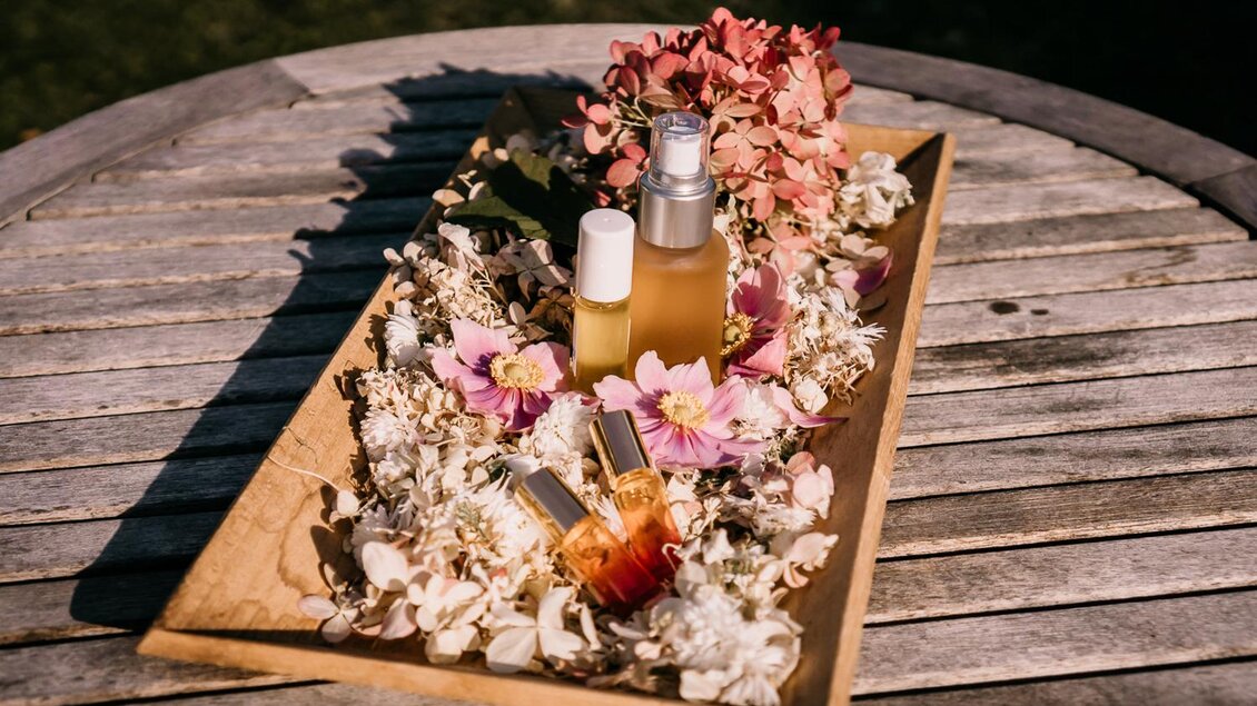 Eine Holzplatte mit zwei Flaschen Pflegeprodukten und bunten Blumen. Die Anordnung strahlt Natürlichkeit und Eleganz aus. | © Petra Stückelschwaiger