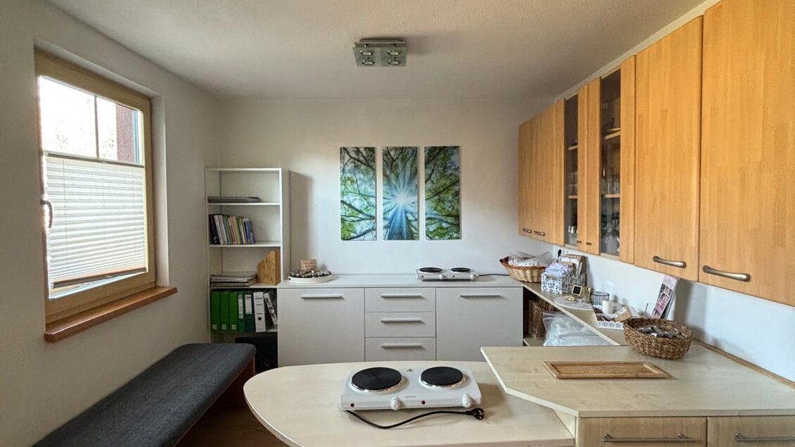 Eine moderne Küche mit Holzschränken und einem runden Esstisch. An der Wand hängen drei Bilder von Pflanzen und es gibt eine gemütliche Sitzbank. | © Petra Stückelschwaiger