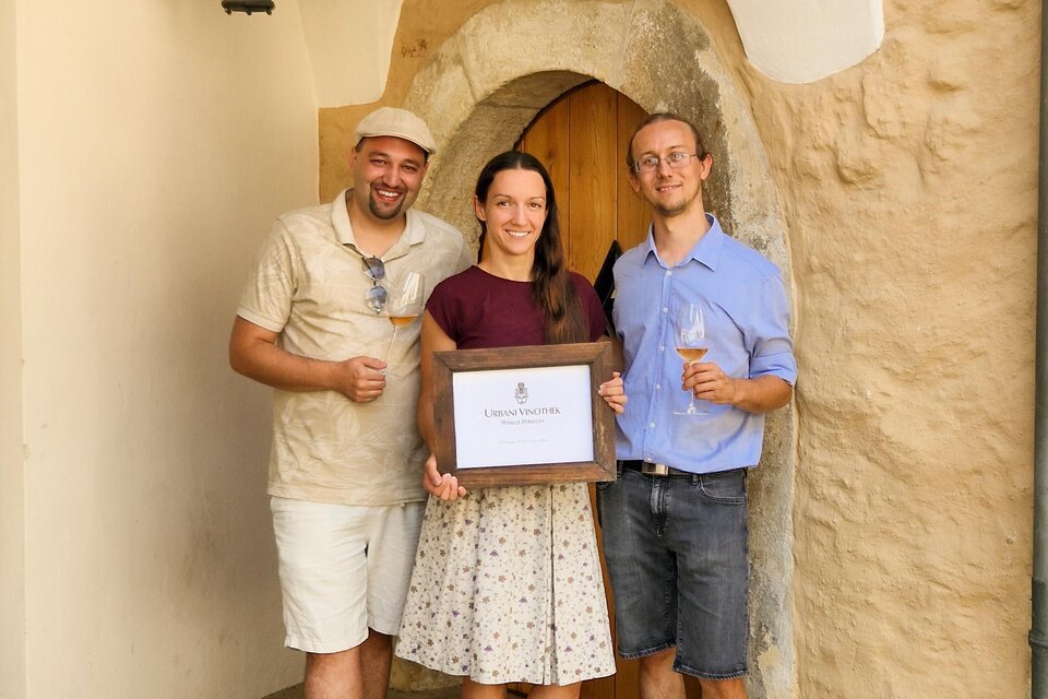 Drei Personen stehen vor einer Tür und halten ein Schild. Sie lächeln und scheinen einen besonderen Moment zu feiern. | © ©Winkler-Hermaden