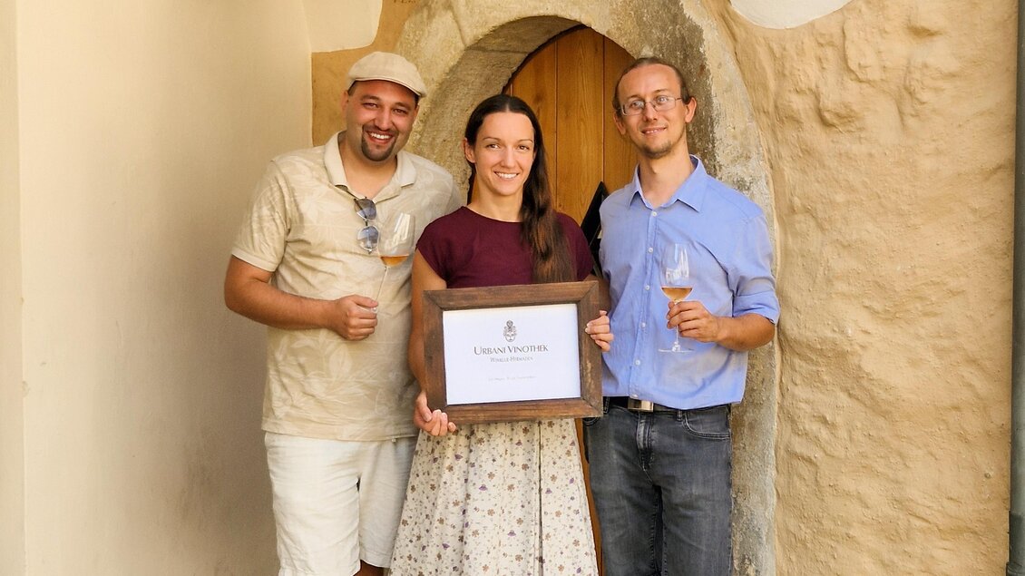 Drei Personen stehen vor einer Tür und halten ein Schild. Sie lächeln und scheinen einen besonderen Moment zu feiern. | © ©Winkler-Hermaden