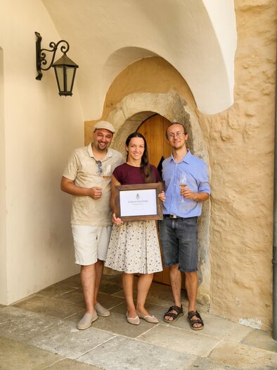 Three people are standing in front of a door holding a sign. They are smiling and appear to be celebrating a special moment. | © ©Winkler-Hermaden