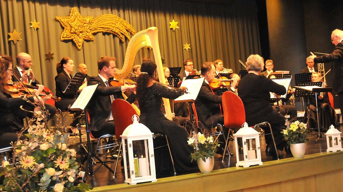 Ein Orchester spielt auf der Bühne. Der Dirigent leitet die Musiker, während dekorative Elemente im Hintergrund zu sehen sind. | © Siegel Sabine
