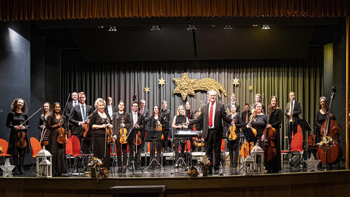 Eine Gruppe von Musikern steht auf einer Bühnen mit verschiedenen Instrumenten. Sie tragen schwarze Kleidung und lächeln in die Kamera.