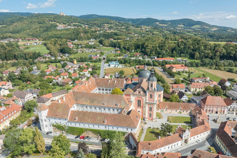 Eine Luftaufnahme eines malerischen Dorfes mit einer großen Kirche und umliegenden Häusern. Die Landschaft ist grün und hügelig, was eine ruhige Atmosphäre vermittelt. | © Helmut Schweighofer