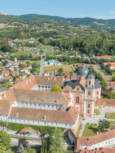 An aerial view of a picturesque village with a large church and surrounding houses. The landscape is green and hilly, conveying a tranquil atmosphere. | © Helmut Schweighofer