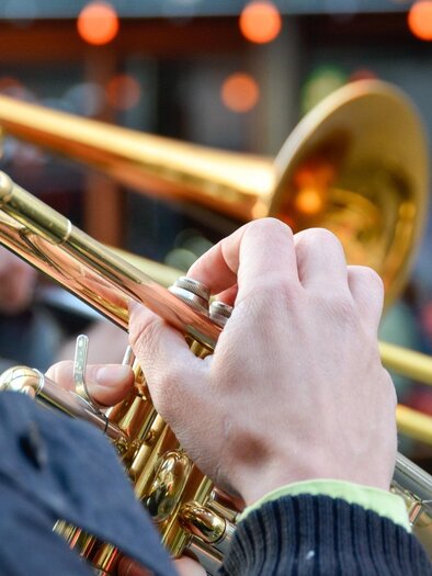 Ein Musiker spielt eine Trompete. Im Hintergrund sind verschwommene Menschen und stimmungsvolle Lichter zu sehen. | © pixabay.com