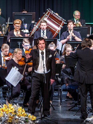 An orchestra is playing on stage while a singer performs in the foreground. In the background, various instruments and musicians can be seen. | © MG Lannach - Petru Rimovetz