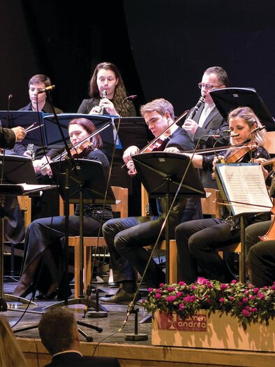 Ein Orchester spielt auf einer Bühne. Der Dirigent leitet die Musiker, die konzentriert notieren. | © Lions Club