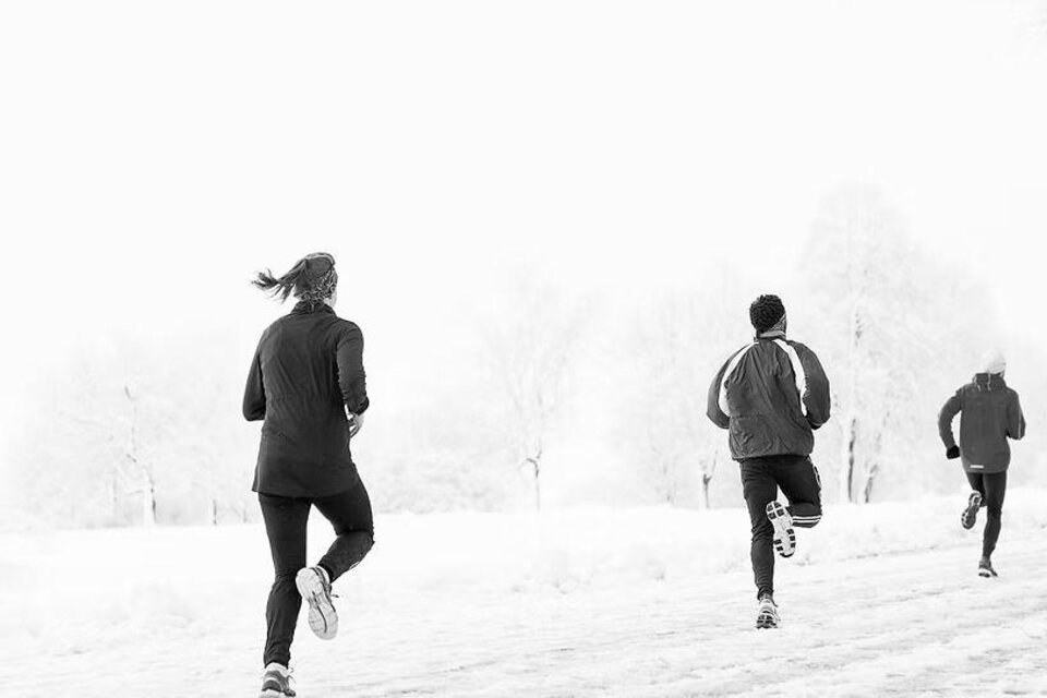 Eine Gruppe von Läufern joggt durch eine verschneite Landschaft. Die Szene ist in Schwarz-Weiß gehalten und vermittelt eine kalte, winterliche Stimmung. | © we.move