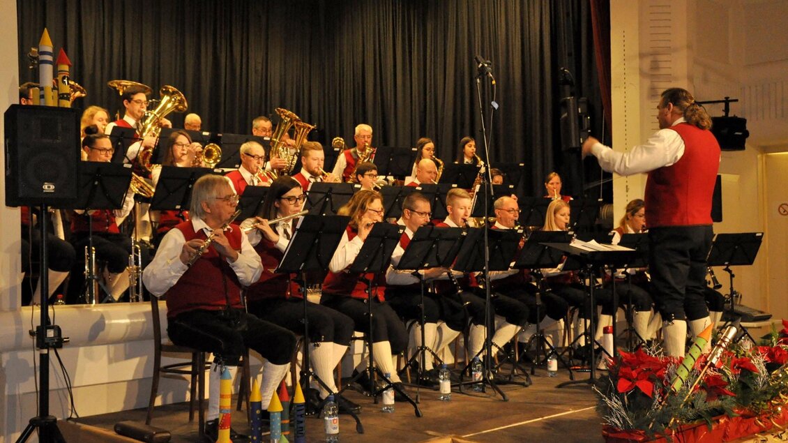 Eine Blaskapelle spielt auf einer Bühne. Der Dirigent leitet die Musiker in traditioneller Tracht. | © GTK Mureck