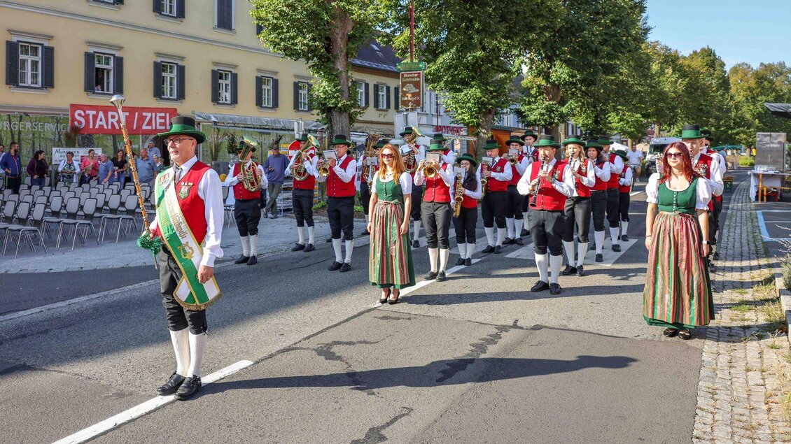 Eine festliche Parade mit Menschen in traditionellen Trachten. Sie marschieren auf einer Straße, umgeben von Bäumen und Zuschauern. | © Foto de Monte