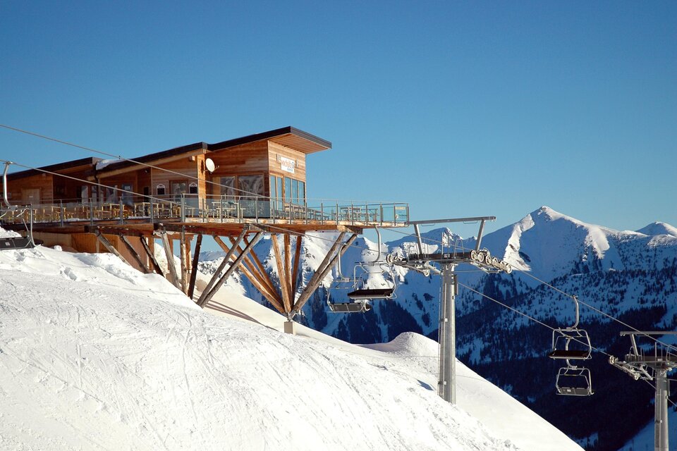 Eine moderne Hütte auf einem verschneiten Berg. Im Hintergrund sind majestätische Berge und ein klarer blauer Himmel zu sehen. | © Riesneralm Bergbahnen/Erwin Petz