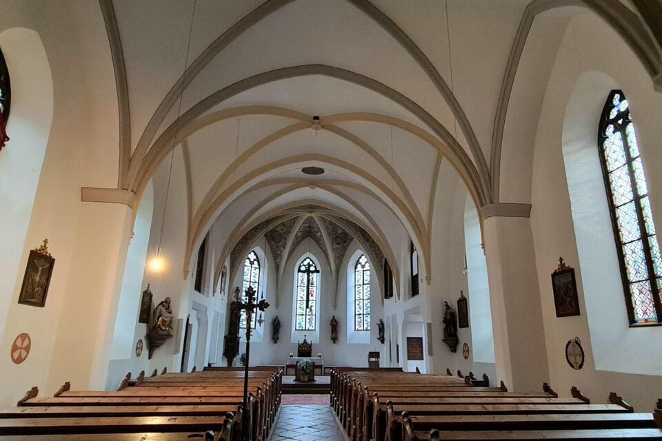 Eine künstlerische Innenansicht einer Kirche mit gewölbten Decken und alten Holzbänken. Die bunten Fenster lassen sanftes Licht in den Raum strömen. | © Stephanie Bor