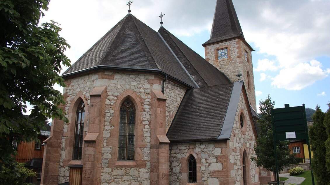 Eine schöne steinerne Kirche mit einem hohen Turm. Sie hat große Fenster und liegt in einer grünen Umgebung. | © Viola Lechner