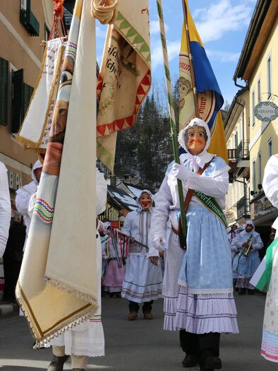 Eine festliche Parade mit Personen in traditionellen Gewändern und Masken. Sie tragen Fahnen und bewegen sich durch eine Straße. | © TVB Ausseerland - Salzkammergut_Zink