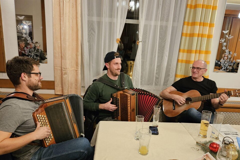 Zwei Musiker sitzen an einem Tisch und spielen traditionelle Musik. Der Mann links spielt Gitarre und der Mann rechts hat ein Akkordeon. | © Familie Nöhrer